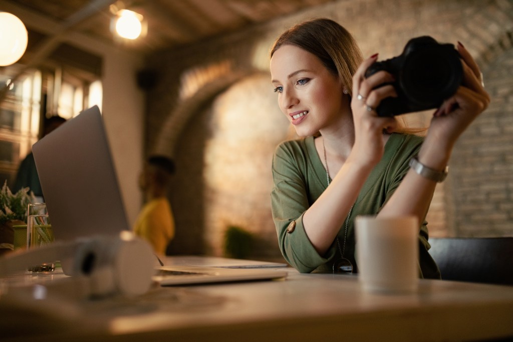 Young woman with digital camera using computer while working late in her studio.